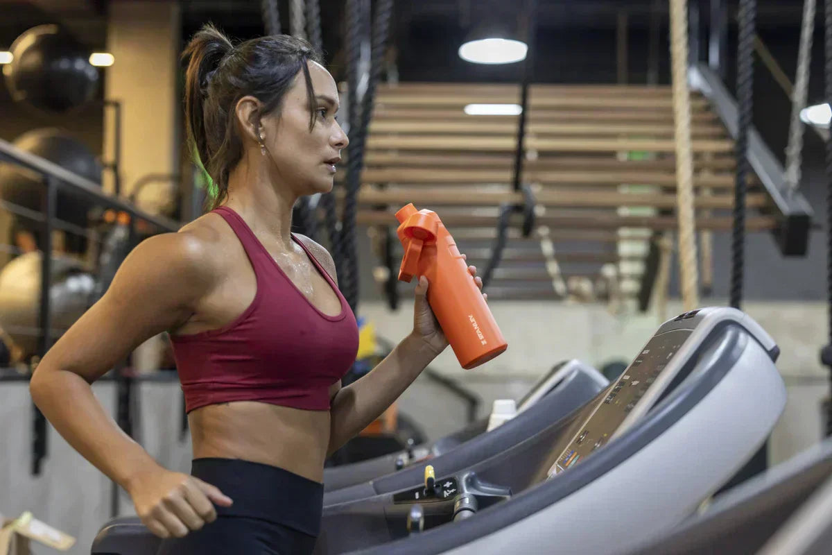 Uma mulher correndo na esteira usando a garrafa Stanley que ela comprou pensando no Dia do Esportista.