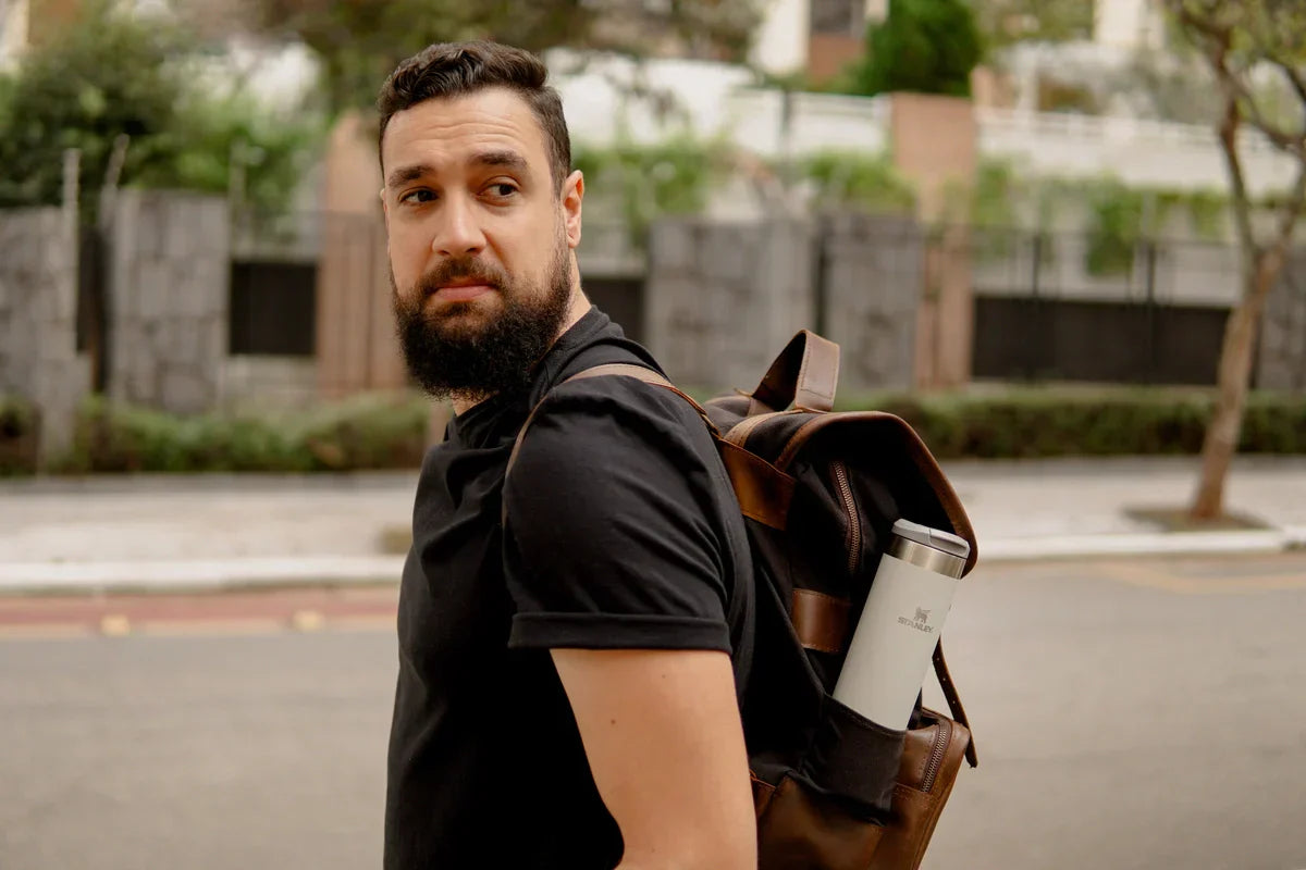 Um homem com uma mala nas costas e uma garrafa Stanley, pronto para aproveitar o Dia Nacional do Turismo.