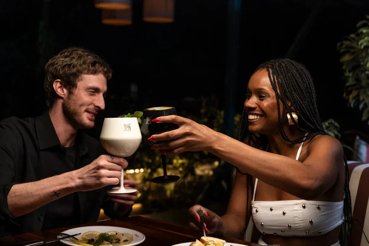 Duas pessoas sorrindo e brindando com seus drinks sem álcool.