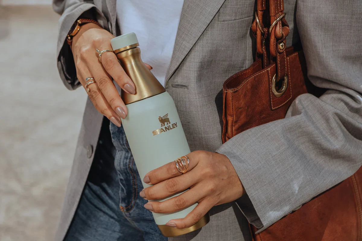 Uma mulher segurando uma garrafa Stanley que ela está levando durante a viagem nas férias de julho para manter a hidratação em dia.