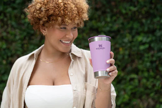 Uma mulher levantando o copo Stanley e sorrindo, por saber como usar cada um dos nossos produtos.