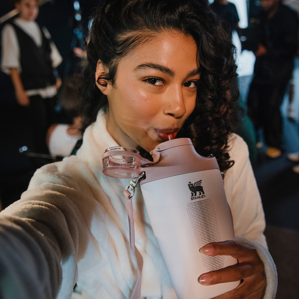 Mulher bebendo em uma garrafa térmica rosa e branca com canudo e alça.